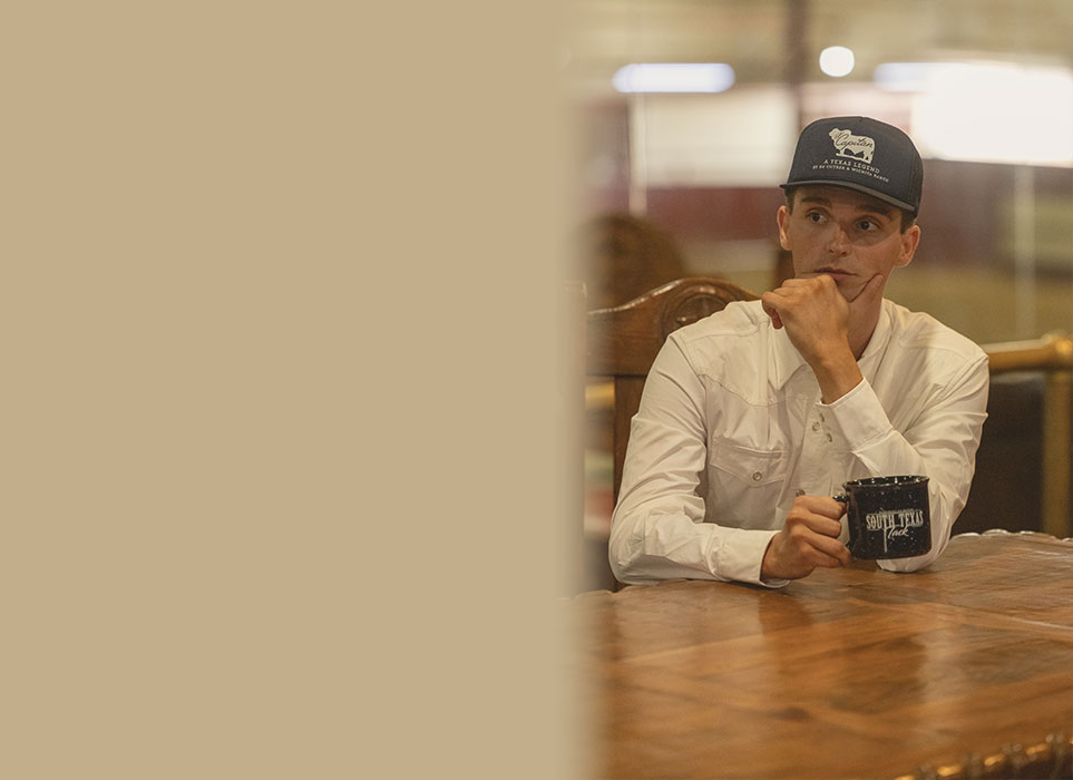 Chad sitting with cap and long sleeve shirt drinking out of south texas tack coffee cup